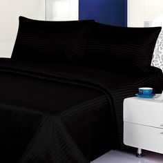 a bed with black bedspreads and pillows on top of it next to a night stand