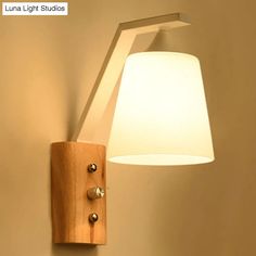 a light that is on the wall next to a lamp with a wooden frame and white shade