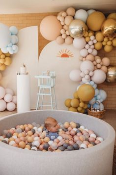 a baby in a tub filled with rocks next to balloons and a wall hanging from the ceiling