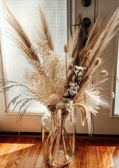 a vase filled with dry grass and rocks on top of a wooden floor next to a door