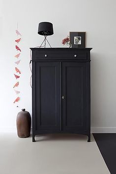 a black cabinet sitting in the corner of a room next to a lamp and vase