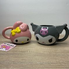 two hello kitty mugs sitting next to each other on top of a wooden table