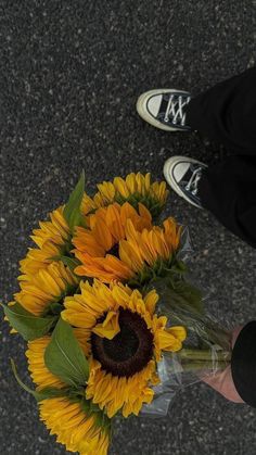 a bouquet of sunflowers on the ground with someone's feet in the background