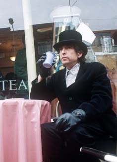 a man wearing a top hat and holding a coffee cup in front of a store window