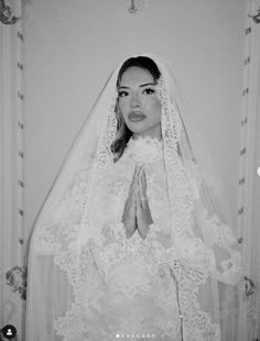 a woman in a wedding dress with her hands clasped up to her chest and wearing a veil over her head