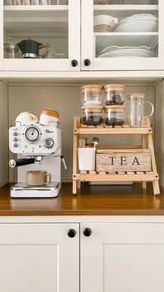 a kitchen with white cupboards and wooden shelves filled with dishes, coffee maker and cups