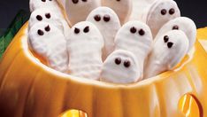 a group of white ghost cookies in a pumpkin bowl with googly eyes on them