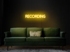 a green couch in front of a black wall with a neon sign that reads recording