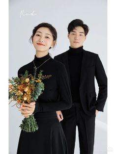 two people standing next to each other with flowers in their hands and one person wearing a black suit