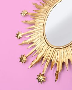 a mirror that is sitting on top of a pink surface with gold stars around it