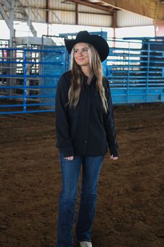 a woman standing in the middle of a dirt field wearing a cowboy hat and jeans