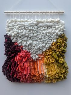 a piece of art made out of yarn on a white wall hanging from a wooden hanger