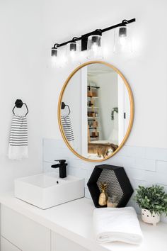 a bathroom with a round mirror above the sink and white countertop, next to a black and white towel rack