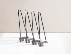 three pairs of metal hooks on a white surface with shadows from the wall behind them