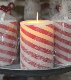 two red and white striped candles sitting on top of a metal tray next to ice