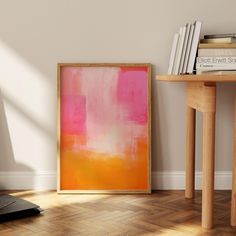 an orange and pink painting sitting on top of a wooden floor next to a table