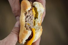 a hand holding a half eaten sandwich with meat and mustard on it's bun