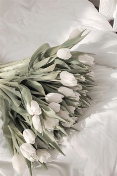 a bouquet of white tulips is laying on a bed with the sheets pulled back