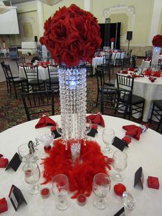 a centerpiece with red flowers and feathers on a table at a formal function in a banquet hall