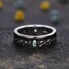 a wedding band with an emerald stone in the center on top of a granite surface