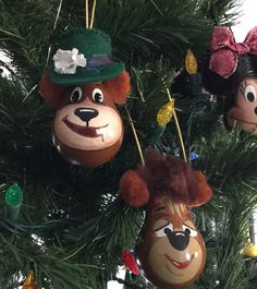 three ornaments are hanging on the christmas tree together, one has a bear head and another has a dog face