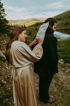 a man and woman standing next to each other on a hill with a paper in their hand