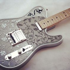 an electric guitar that is decorated with flowers and scrolls on it's body, sitting on a white surface