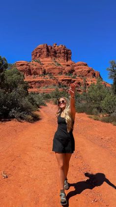 a woman is standing in the middle of a dirt road and raising her arms up