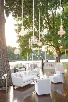 an outdoor seating area with chandeliers hanging from the trees and white couches