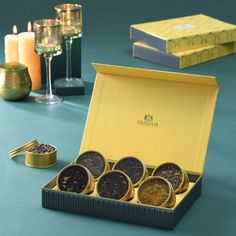 an open box with six different types of teas in it next to some candles