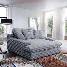 a large gray couch sitting in front of two windows on top of a wooden floor