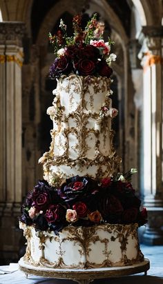 a three tiered wedding cake with flowers on the top and bottom, in front of an archway