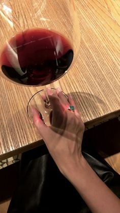 a person holding a wine glass with red wine in it on top of a wooden table