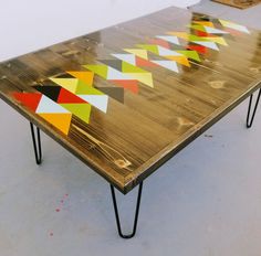 a wooden table with multicolored geometric designs on the top and hairpin legs