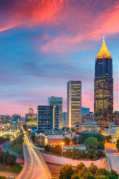 the city skyline is lit up at night with colorful clouds and lights in the sky