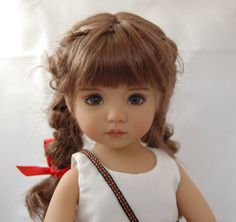 a close up of a doll wearing a white shirt and red ribbon around her neck