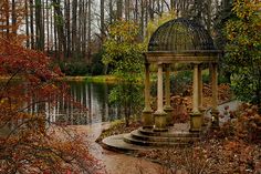 a gazebo in the middle of a park surrounded by water and trees with red leaves