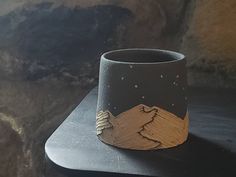 a cup sitting on top of a table next to a stone wall with mountains in the background