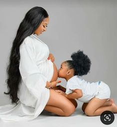 a pregnant woman sitting on the ground next to two small children, both wearing white