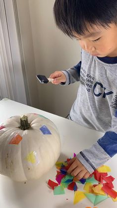 a young boy is painting a pumpkin with colored paper