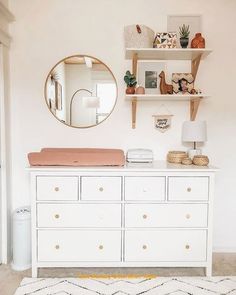 a white dresser topped with drawers and a round mirror above it's top shelf