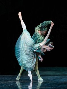 two ballerinas dressed in green tutus and headdress, one holding the other