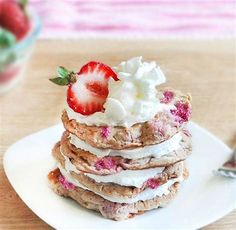 a stack of pancakes topped with whipped cream and strawberries