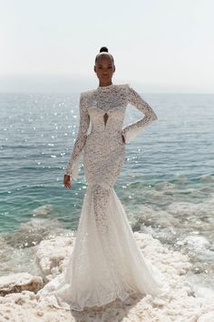 a woman in a wedding dress standing on the rocks by the ocean with her hands on her hips