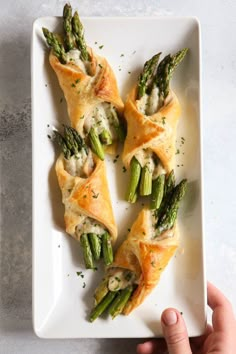 asparagus and cheese pastries on a white plate with a hand reaching for one