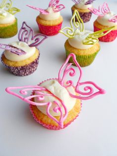 cupcakes decorated with icing and butterflies on white table top next to each other