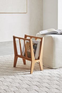 a wooden magazine rack with books on it in front of a white couch and ottoman