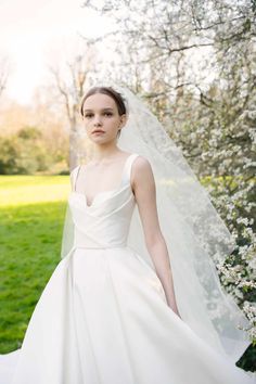 a woman wearing a wedding dress and veil in front of some trees with white flowers