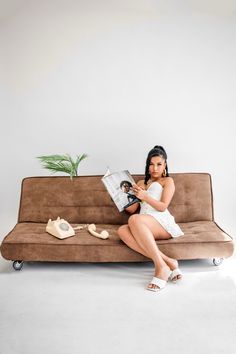 a woman sitting on top of a couch reading a book next to a potted plant