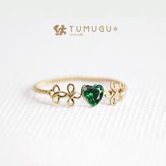 a gold ring with two green heart shaped stones on it's side, and the word